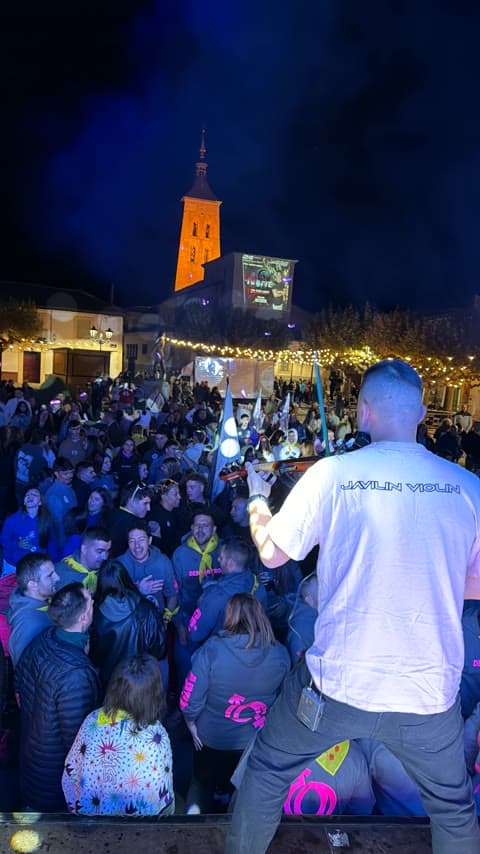 Violinista animando a la plaza del pueblo junto al campanario iluminado durante una actuación de Nostra Notte.
